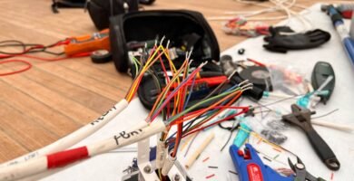 Conjunto de cables multicolores conectados a un conector estanco, herramientas de corte y mediometer en el fondo, mostrando un entorno de trabajo en electrónica naval.