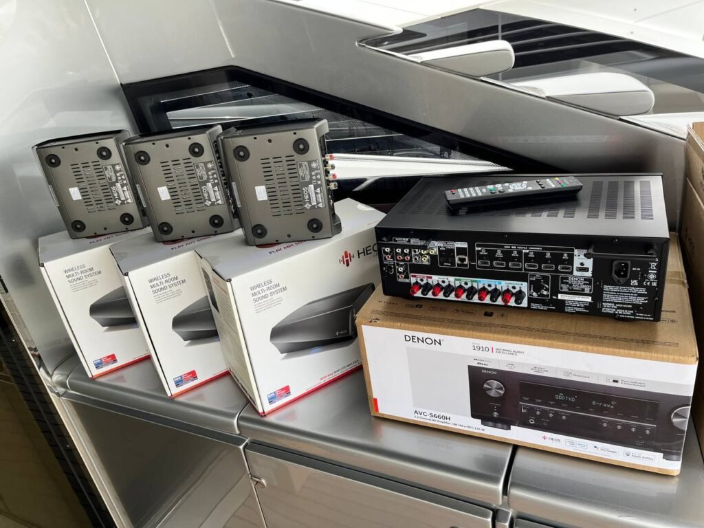 Vista de un sistema de audio inalámbrico compuesto por múltiples altavoces y un receptor Denon destinado a uso en embarcaciones.